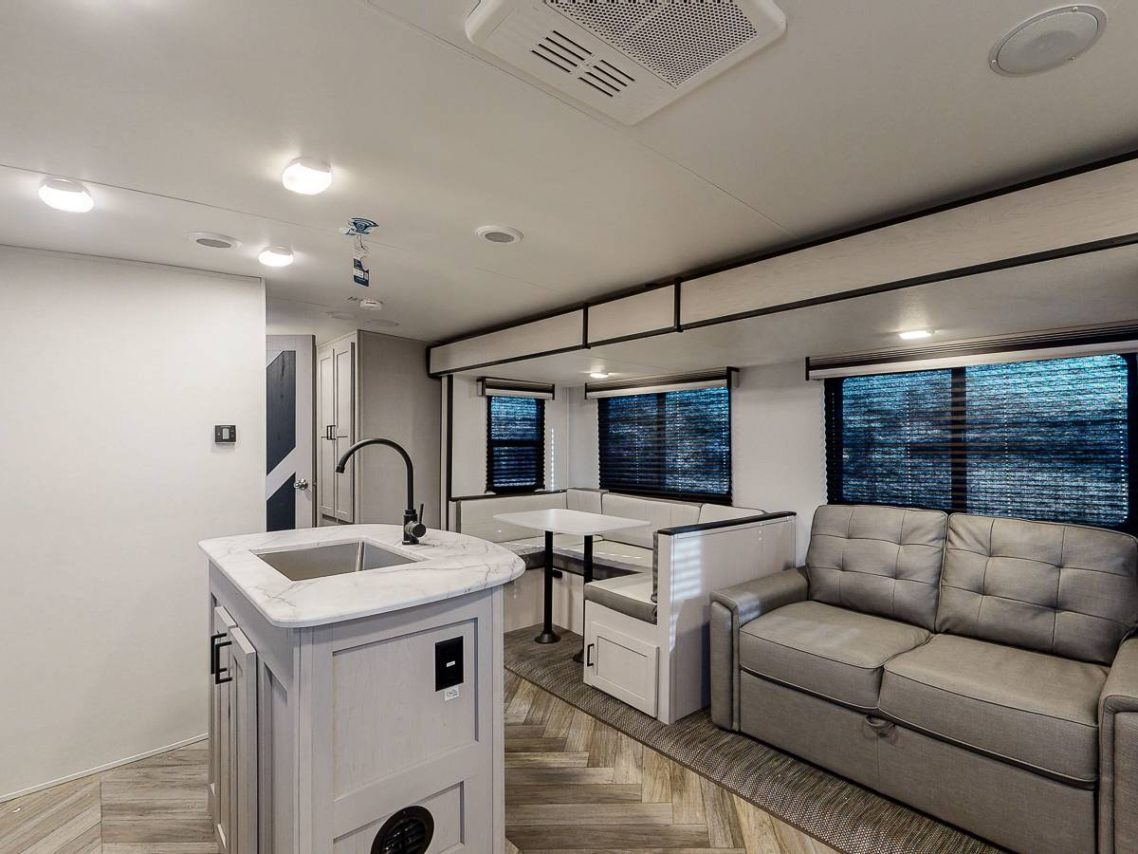 Spacious Living Area Modern, spacious RV interior featuring a kitchen island, sofa, and dining area by windows.